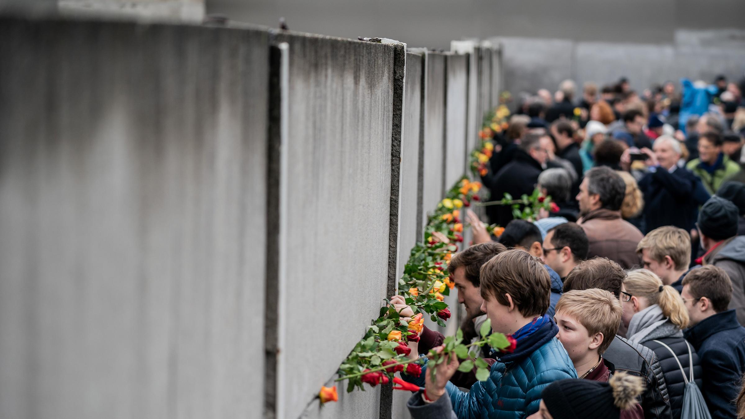 Menschen stecken Rosen in Teile der Berliner Mauer. 