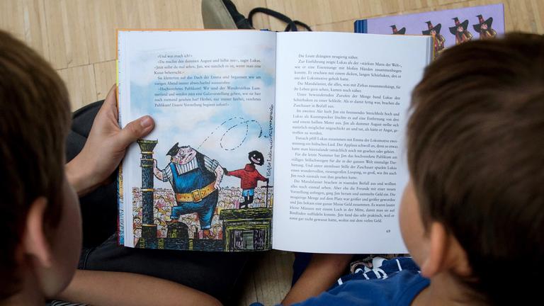Kinder lesen das Buch "Jim Knopf". Auf der Seite sind Illustrationen. 