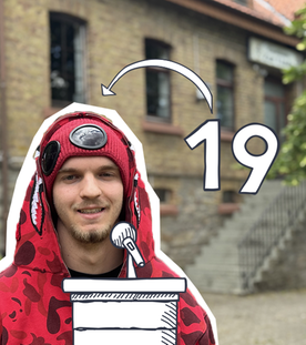 Ein junger Mann im roten Kapuzenpullover vor einem Gebäude.