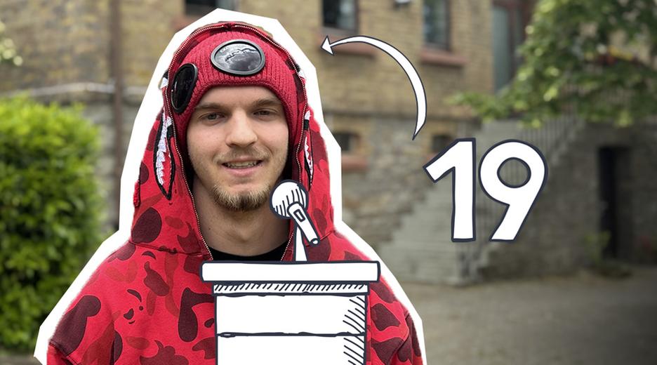 Ein junger Mann im roten Kapuzenpullover vor einem Gebäude.