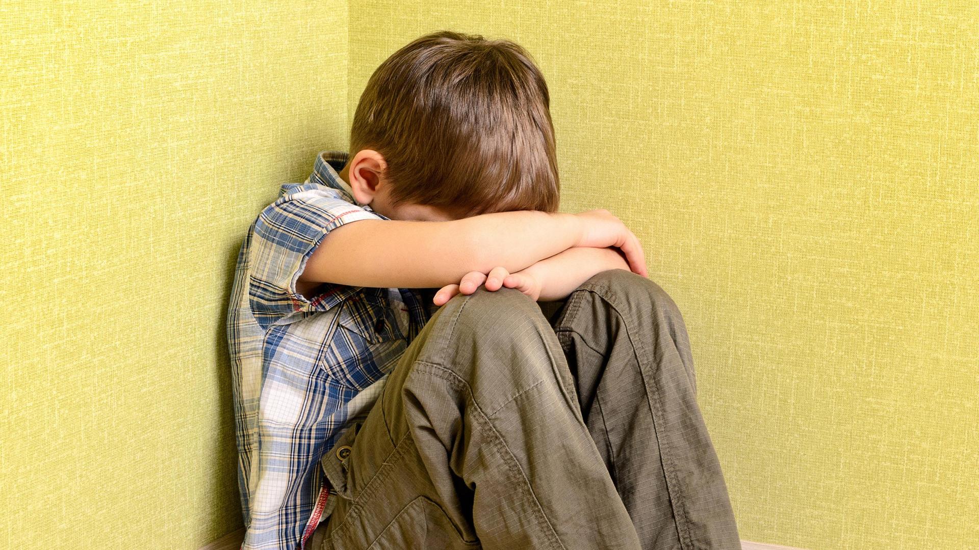 Ein Junge sitzt traurig in der Ecke