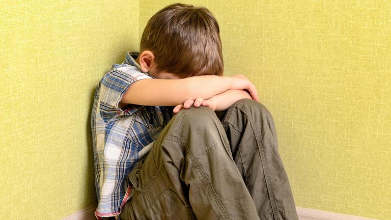 Ein Junge sitzt traurig in der Ecke