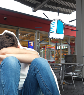 Tankstelle im Hintergrund, im Vordergrund ein Junge, der seinen Kopf auf den Knien abstützt