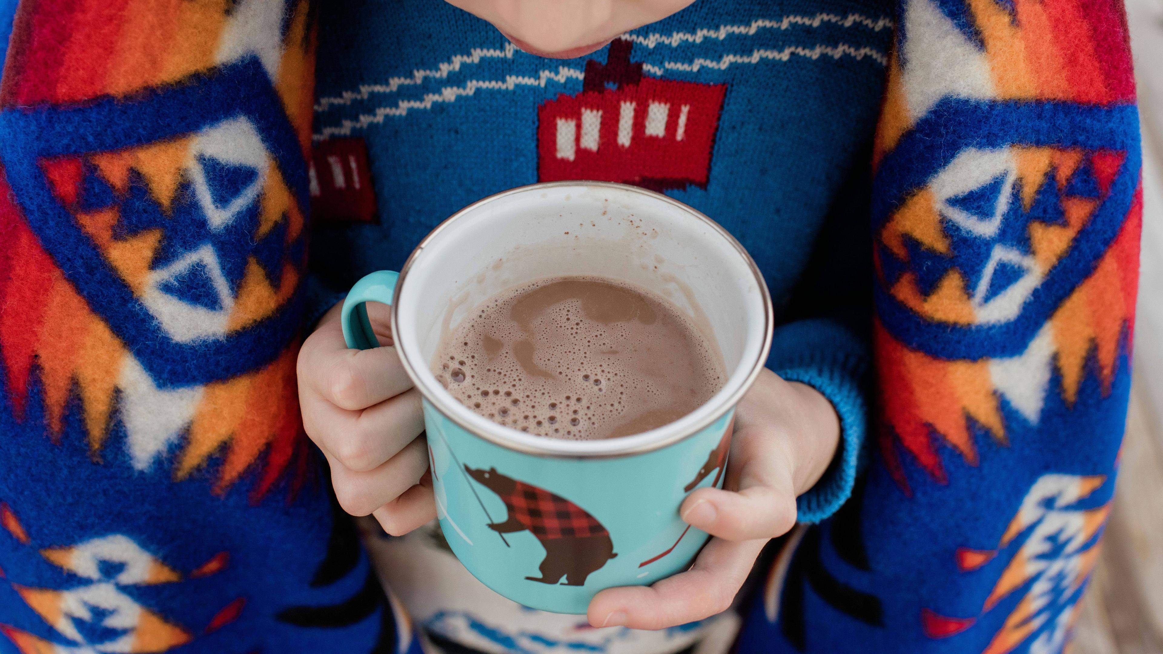 Tasse Kakao in der Hand von einem Kind, es hat eine Decke auf der Schulter 