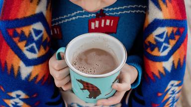 Tasse Kakao in der Hand von einem Kind, es hat eine Decke auf der Schulter 