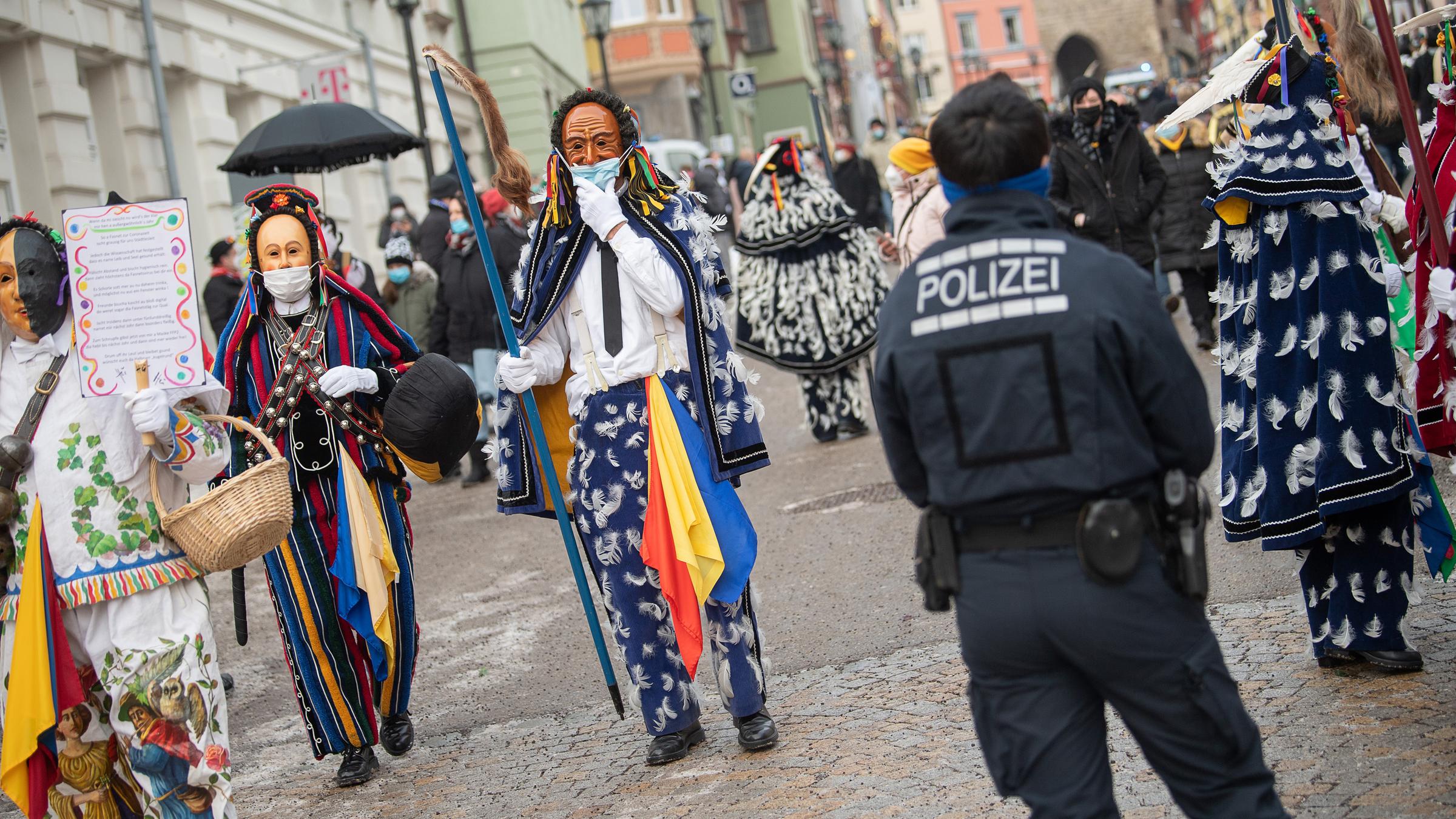 Einige Menschen laufen auf der Straße und tragen dabei Holzmasken und Kostüme.