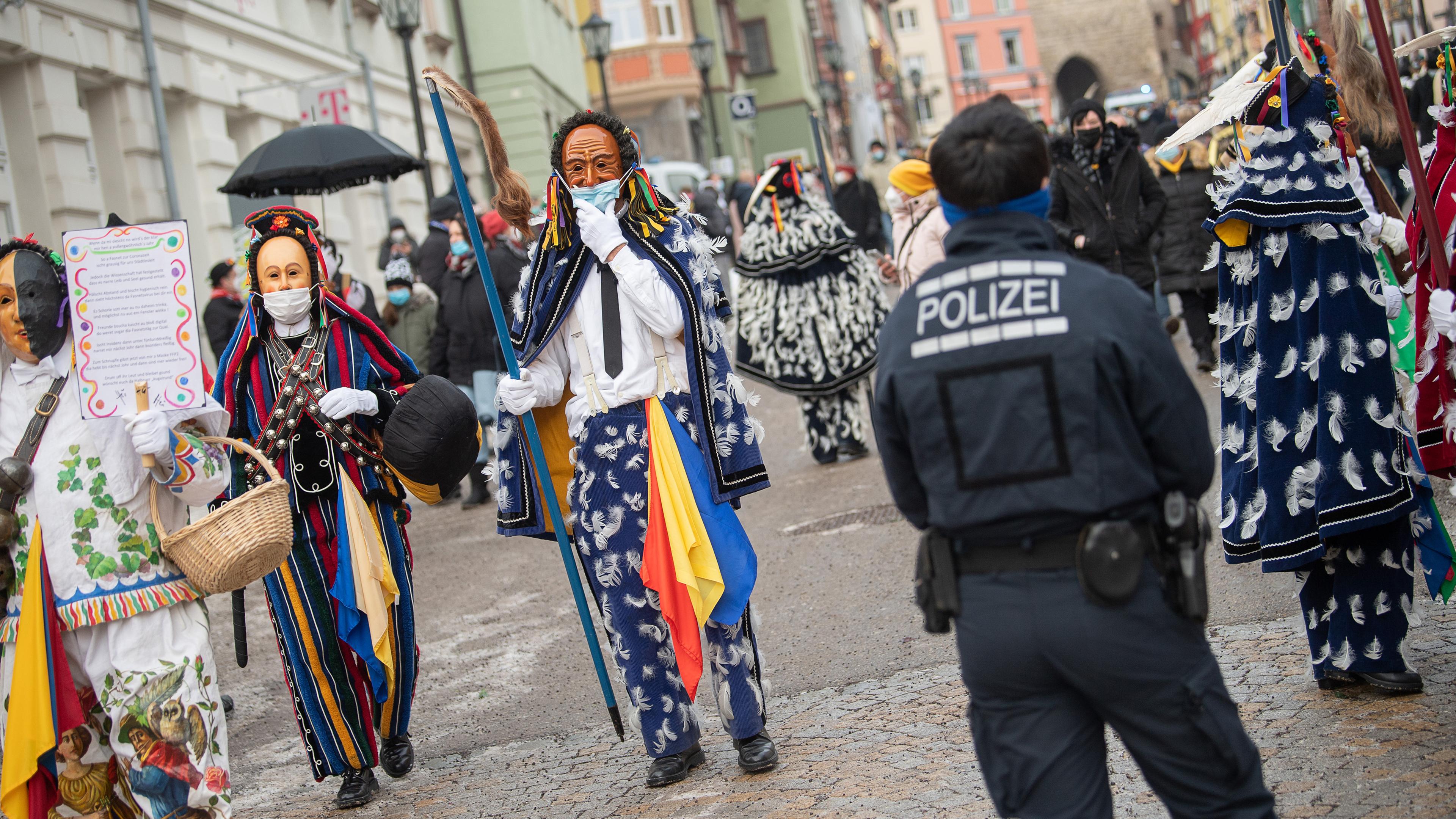 Einige Menschen laufen auf der Straße und tragen dabei Holzmasken und Kostüme.