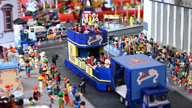 Ein blauer Spielzeug-Umzugswagen fährt zwischen Spielfiguren hindurch.