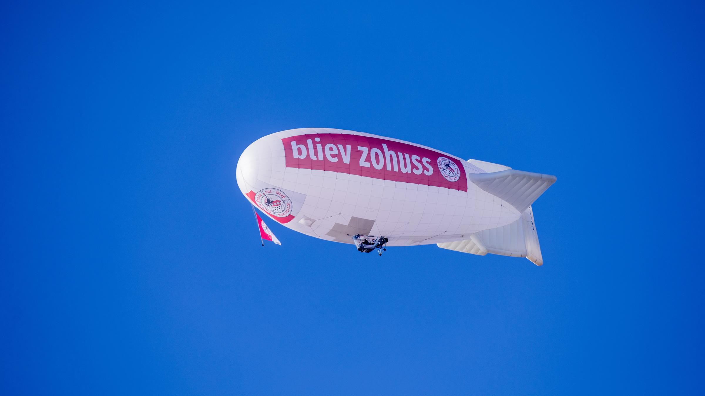 Ein Zeppelin mit der Aufschrift "bliev zohuss", das bedeutet im Kölner Dialekt "bleib zuhause", fliegt über den Spitzen des Kölner Doms.