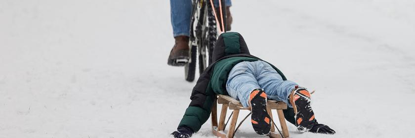 Ein Kind lässt sich am auf einem Holzschlitten von einem Fahrrad über einen verschneiten Weg am Westerberg in Osnabrück (Niedersachsen, Deutschland) ziehen. 