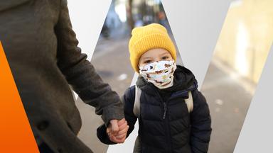 Kind mit Stoffmaske an der Hand der Mutter