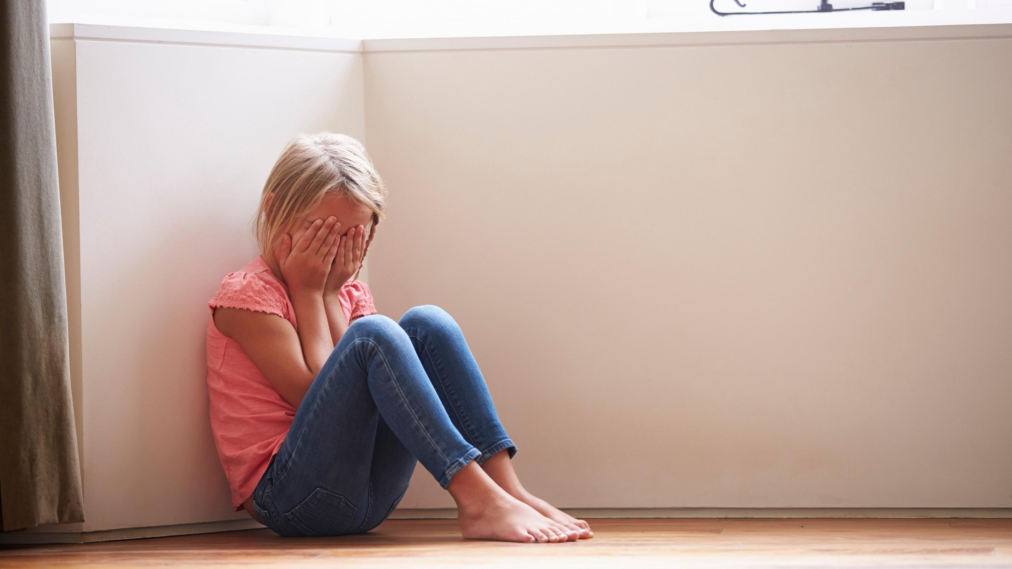 Ein trauriges Mädchen sitzt in einer Ecke. (Symbolbild)