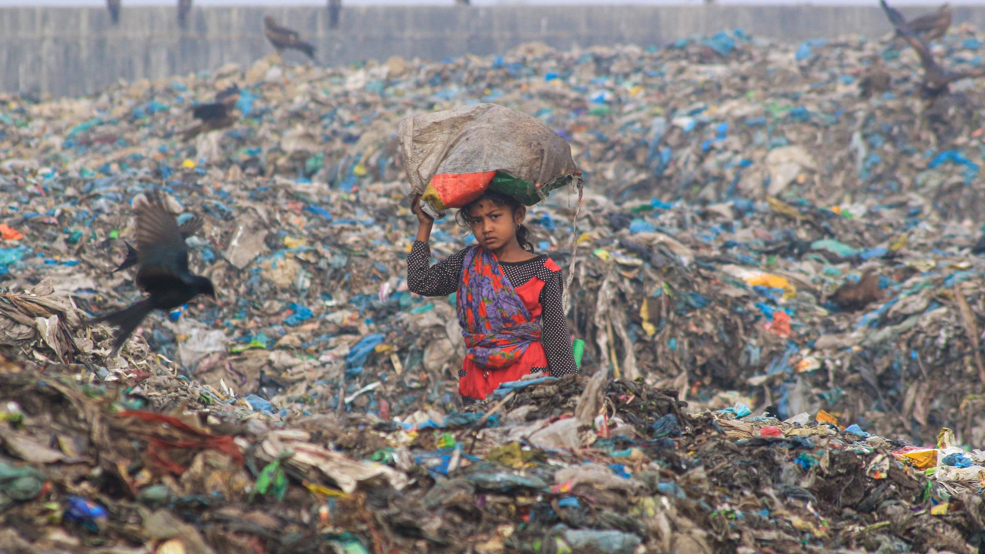 Ein Mädchen arbeitet auf einer Mülldeponie und trägt einen Sack über dem Kopf.