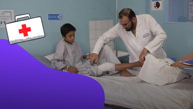 Ein Mann versorgt einen Jungen auf einer Liege in einem Krankenhauszimmer.