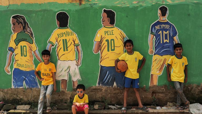 Kinder posieren vor Wandgemälden mit Motiven zur FIFA-Weltmeisterschaft, die an den Wänden des Stadtteils Bahaddarhat Khatib Para in Chattogram, Bangladesch, zu sehen sind.