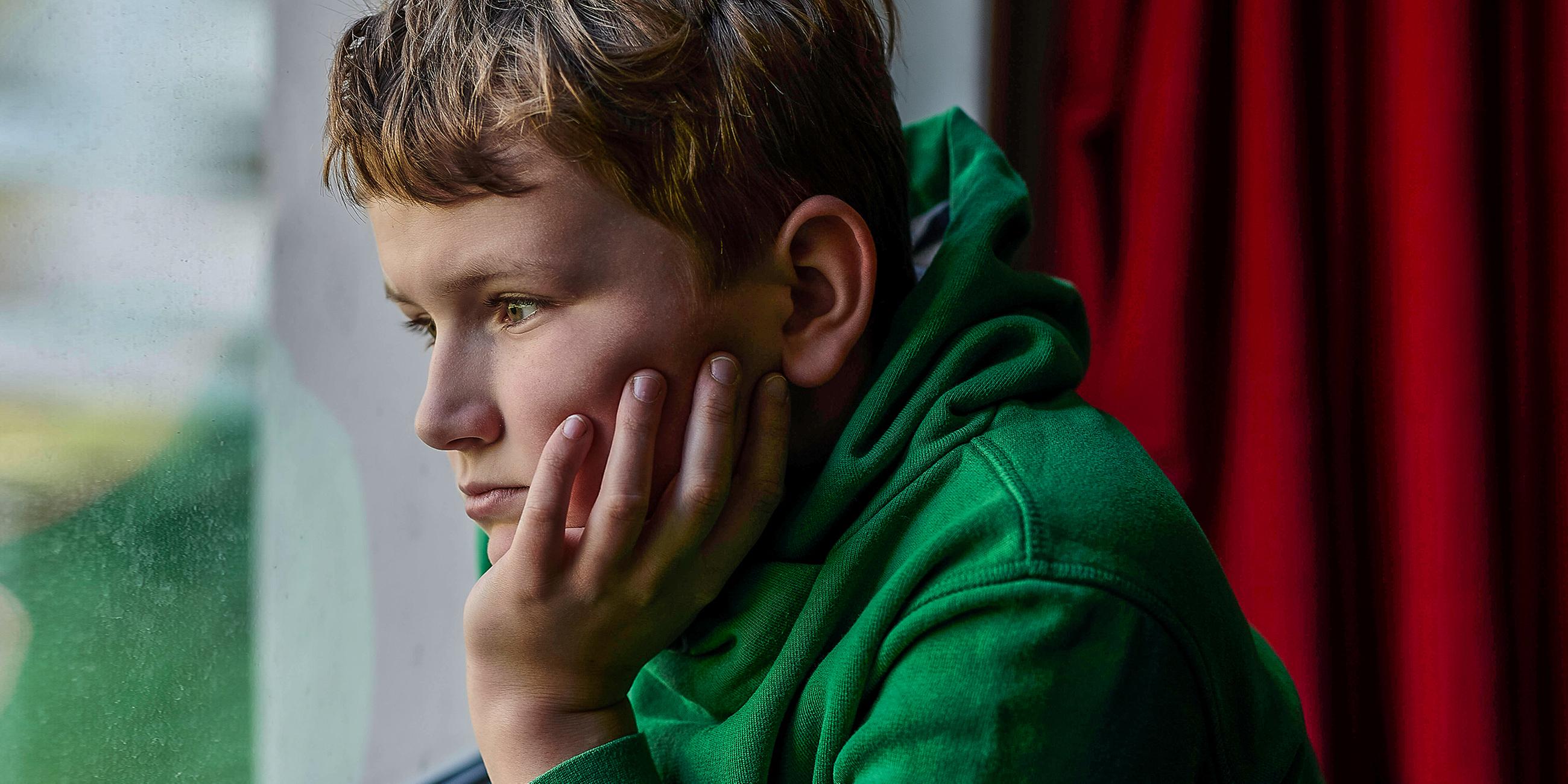 Junge schaut traurig aus dem Fenster