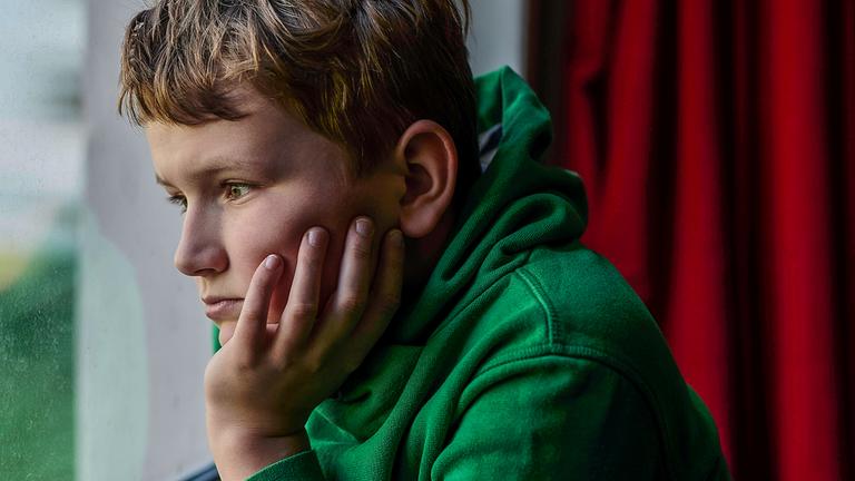 Junge schaut traurig aus dem Fenster