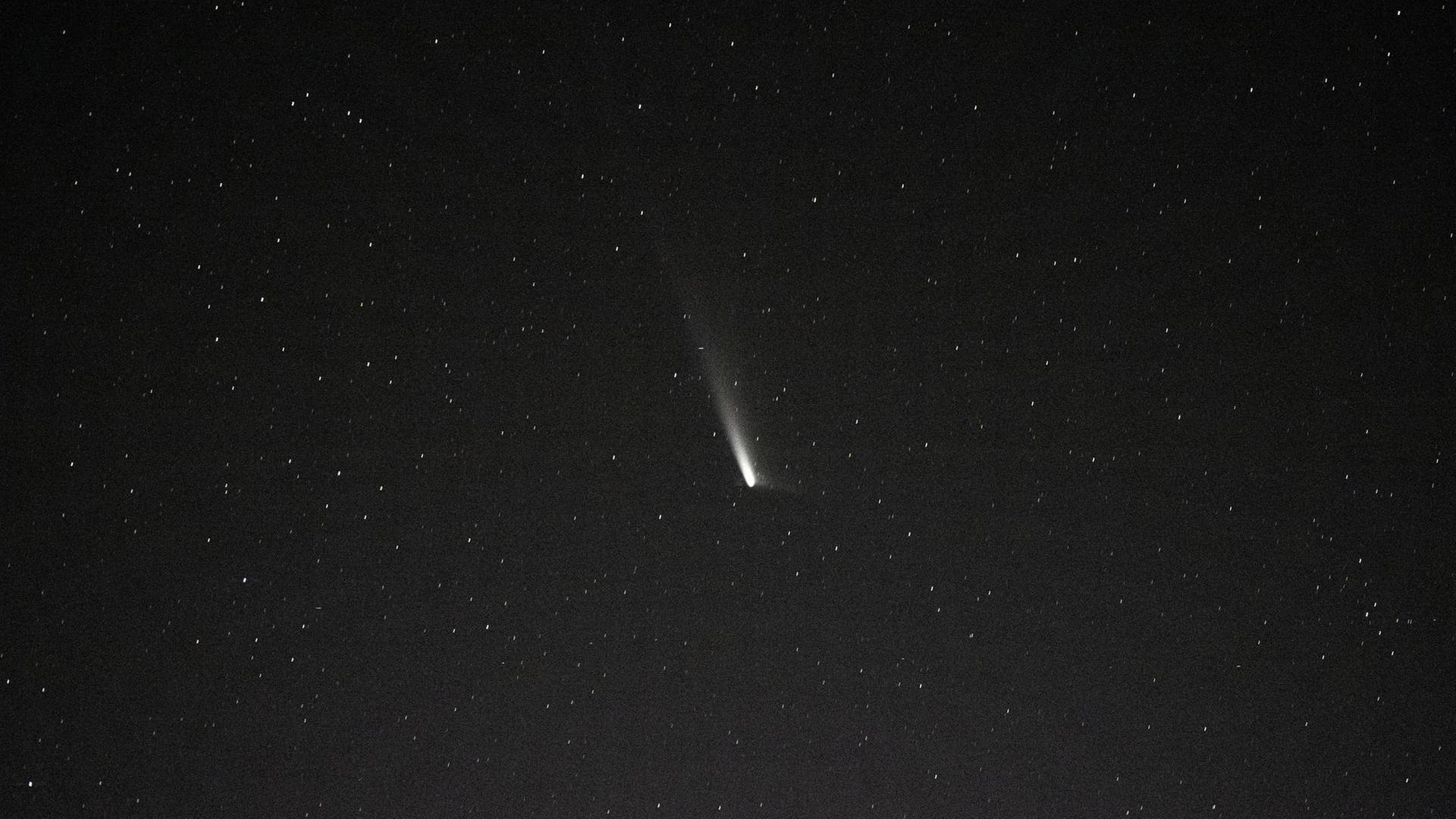 Ein Komet mit Schweif am dunklen Sternenhimmel. 