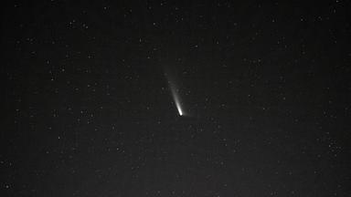 Ein Komet mit Schweif am dunklen Sternenhimmel. 