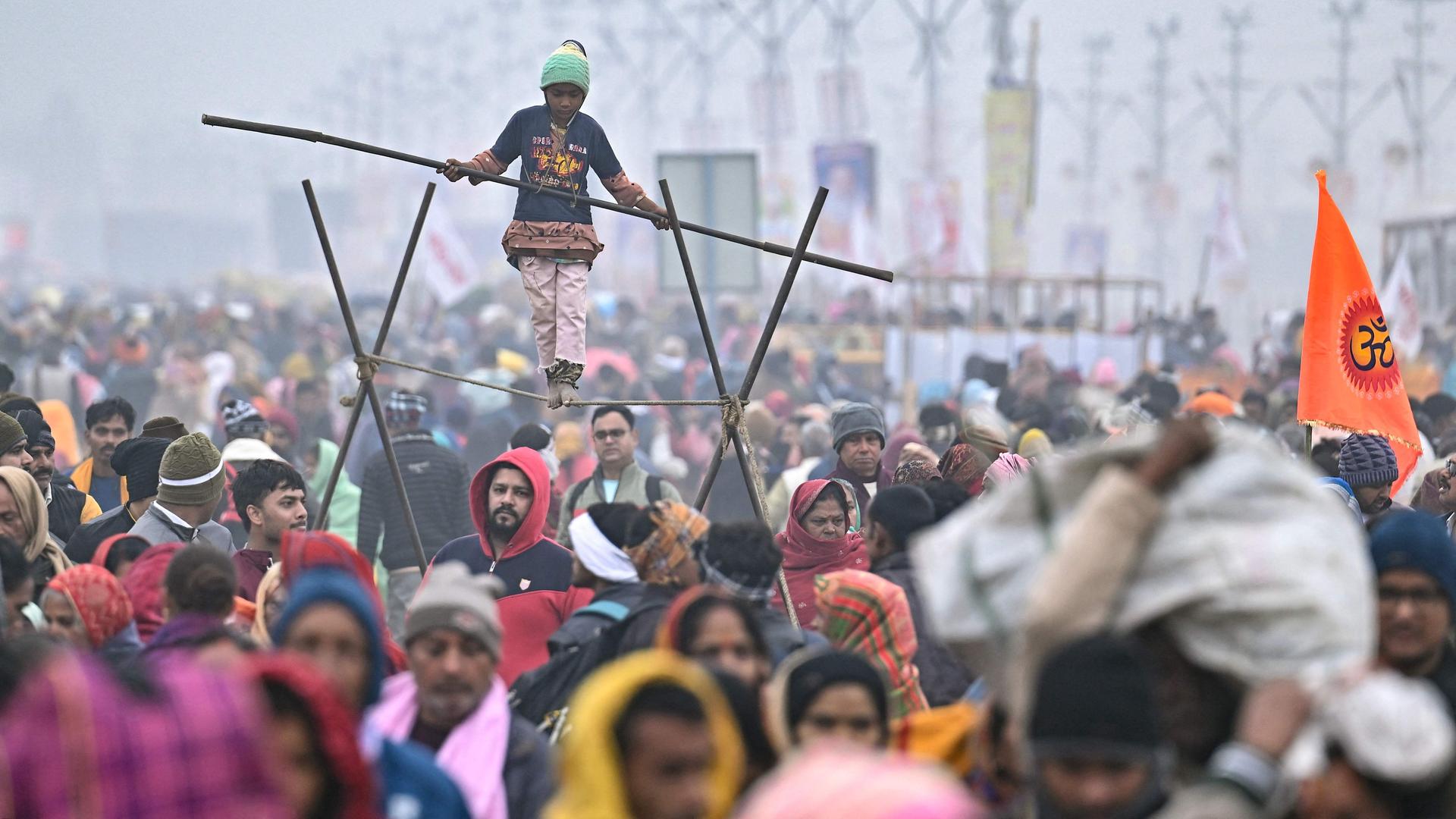 Große Menschenmenge bei nebligem Wetter, in der Mitte balanciert ein Kind auf einem Seil.