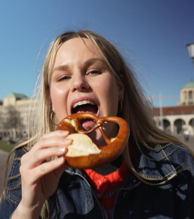 Reporterin Isabelle beißt im Sonnenschein in eine Breze.
