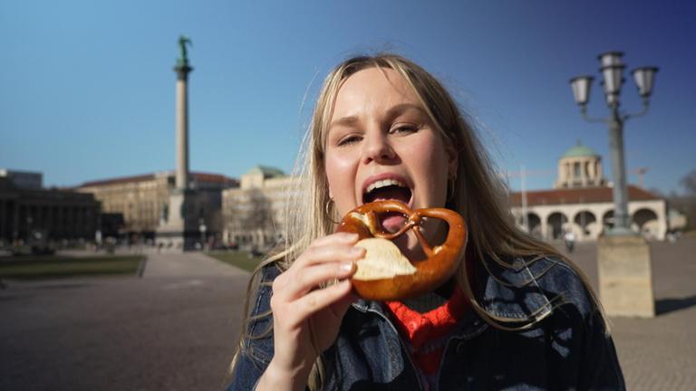 Reporterin Isabelle beißt im Sonnenschein in eine Breze.