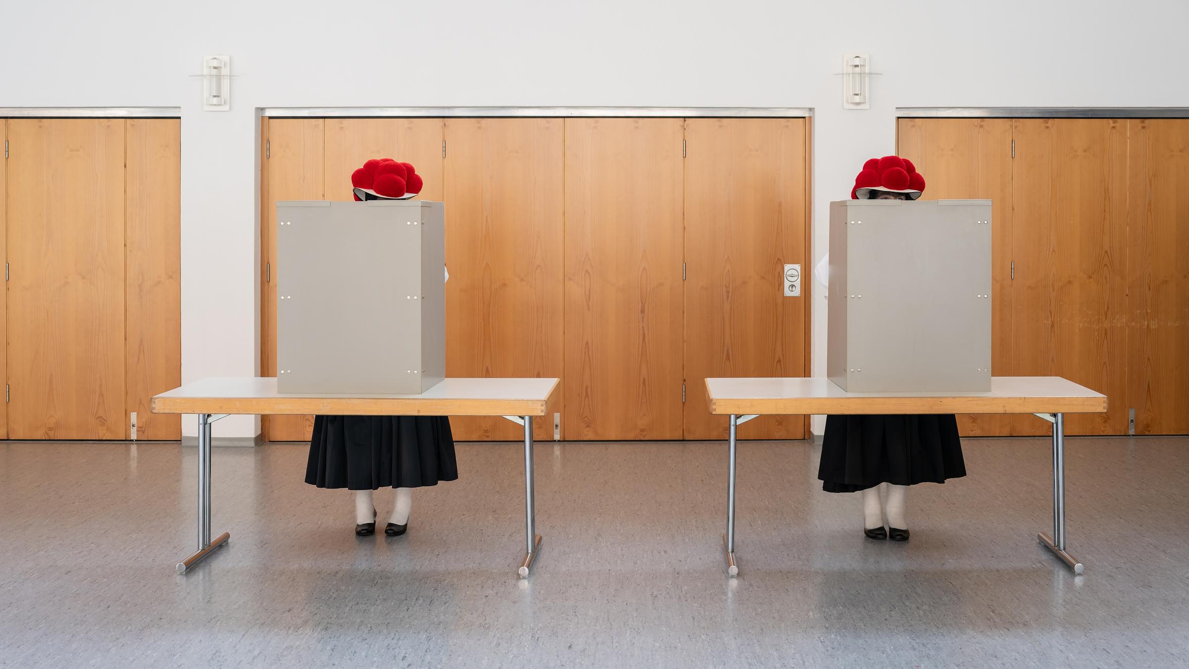 Zwei Frauen stehen in ihrer traditionellen Schwarzwälder Tracht mit rotem Bollenhut im Wahllokal und geben ihre Stimme für die Landtagswahl ab.