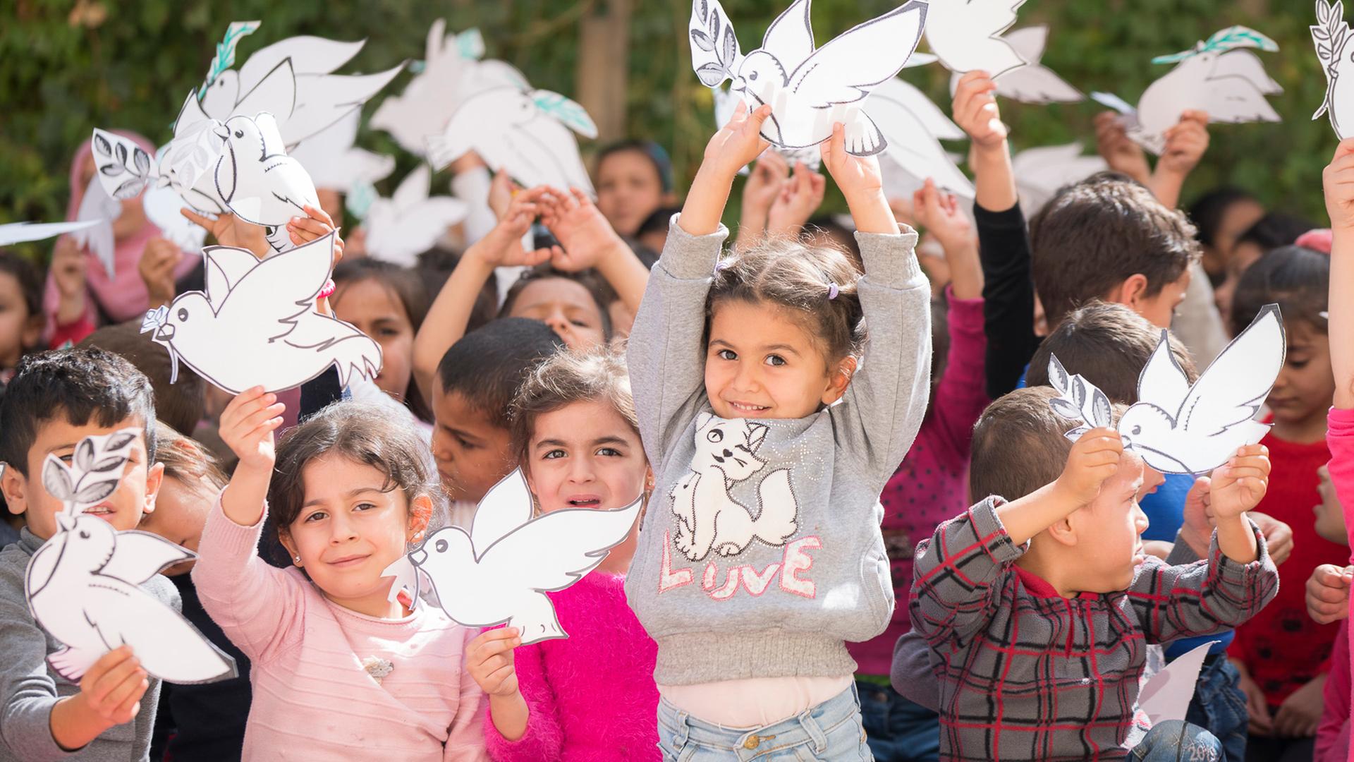 Die schönsten Weihanchts-Hits: Kinder halten Friedenstauben aus Papier in den Händen