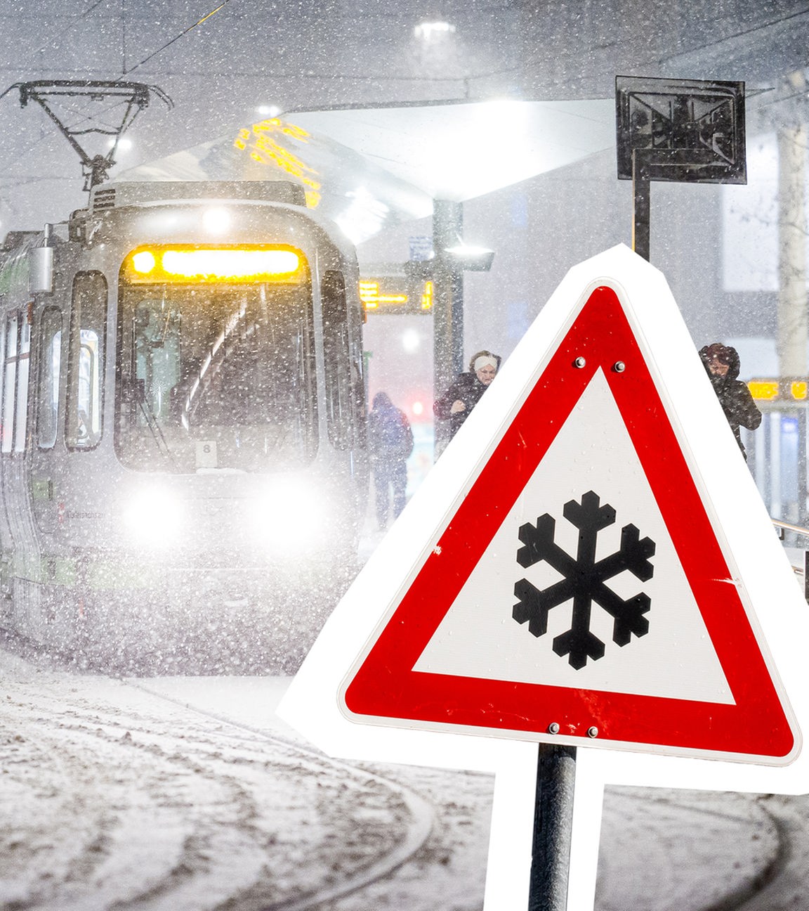  Eine Straßenbahn hält am frühen Morgen im dichten Schneefall an einer Haltestelle daneben ist ein Warnschild mit einer Schneeflocke