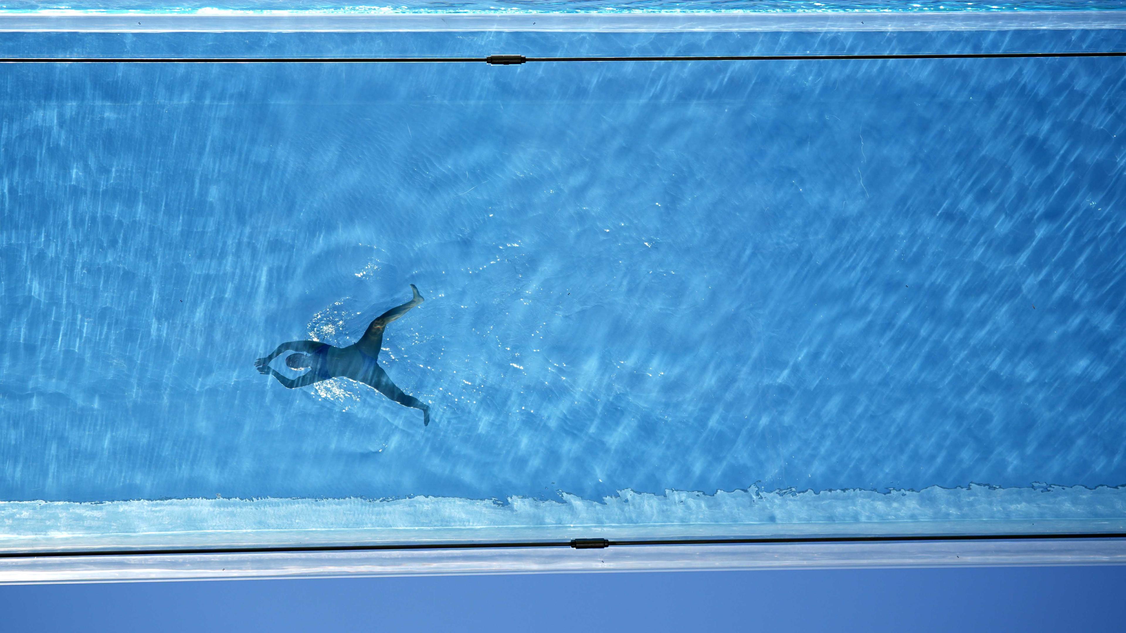 Ein Schwimmer im Sky Pool, einem transparenten Schwimmbecken, das 35 Meter über dem Boden zwischen zwei Wohngebäuden aufgehängt ist, während des heißen Wetters in Nine Elms im Zentrum Londons, wo die dritte Hitzewelle des Sommers das Vereinigte Königreich trifft und die Temperaturen über das Wochenende hoch bleiben sollen. 
