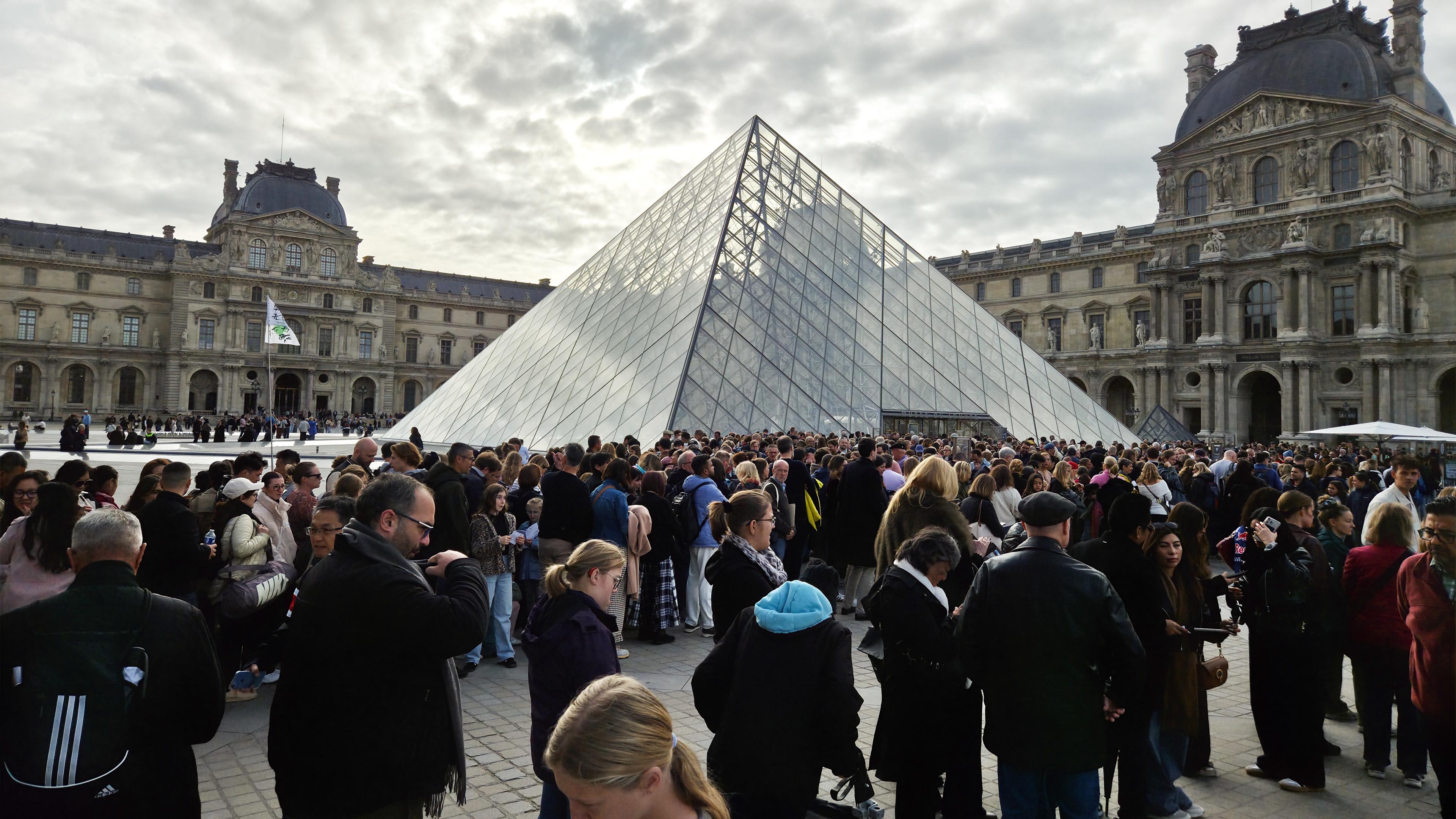 Viele Menschen warten vor dem Louvre in Paris. 
