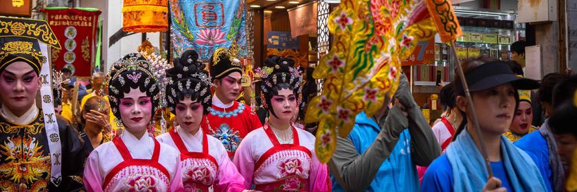 Bunt verkleidete Menschen mit Fahnen ziehen durch eine Straße in Macao in China. 