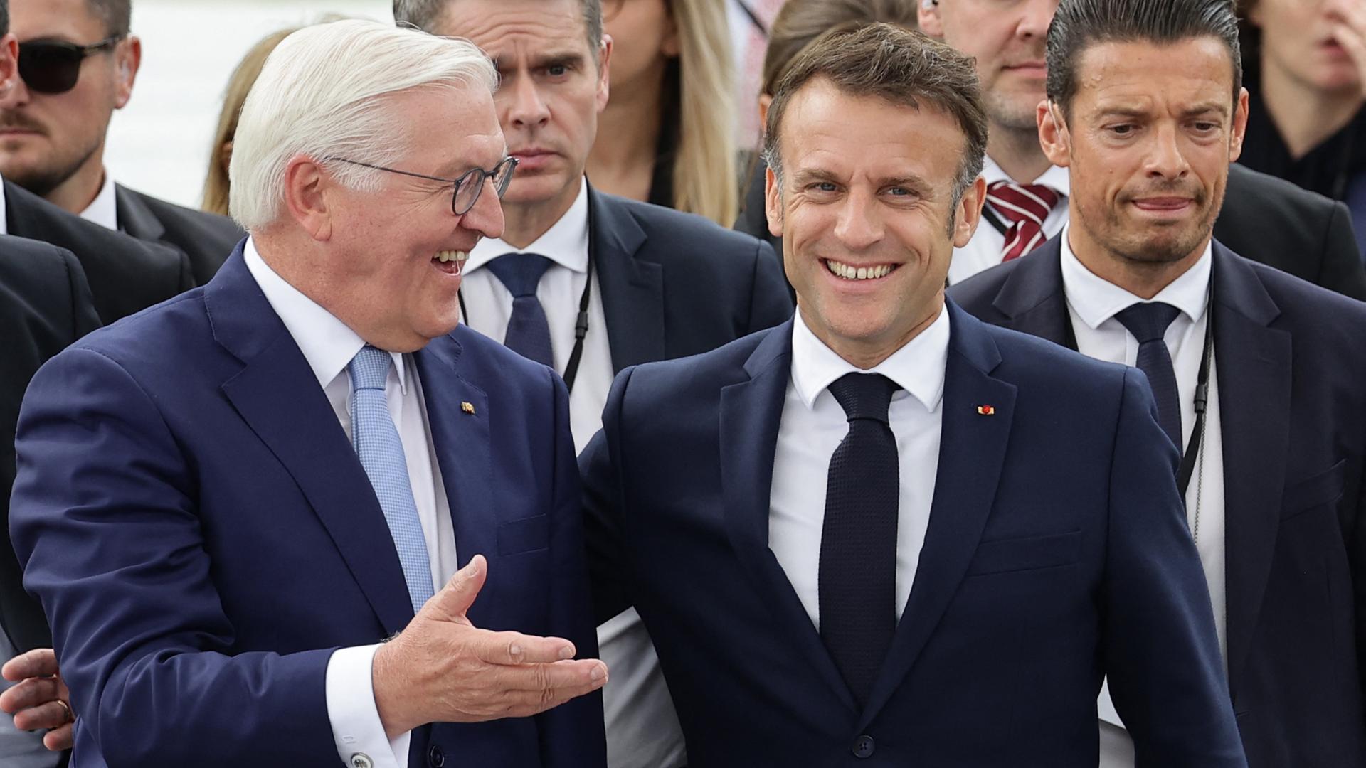 Bundespräsident Steinmeier (links) und der französische Präsident Emmanuel Macron (rechts) umarmen sich und lachen in die Kamera. 