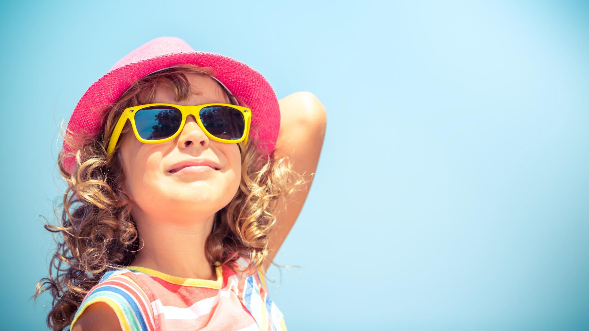 Mädchen mit Sonnenhut und Sonnenbrille schaut zufrieden Richtung Sonne