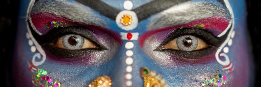 Ein Mann mit blau geschminktem Gesicht, auffälligen Nasenpiercings und weißen Verzierungen. 