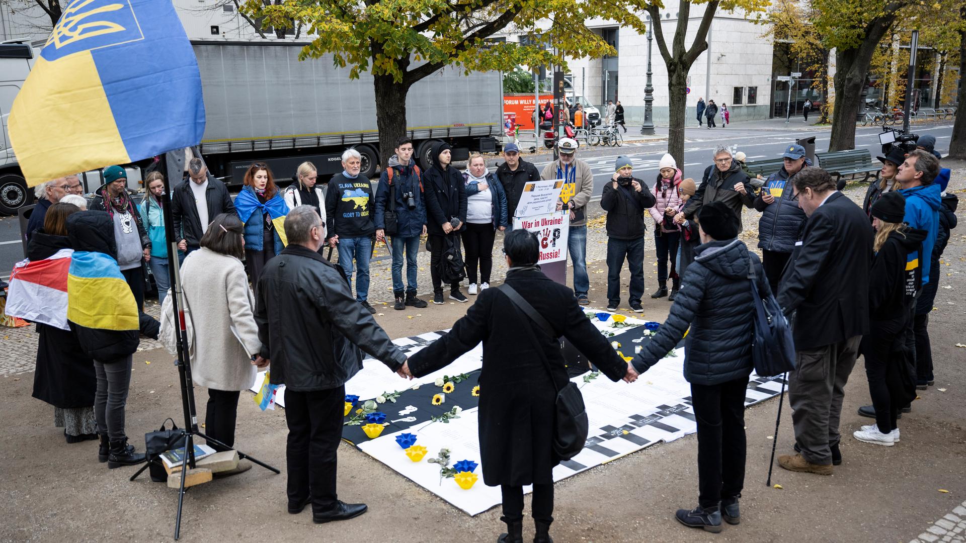 Teilnehmer einer Mahnwache für ukrainicshe Kinder halten sich die Hände. 