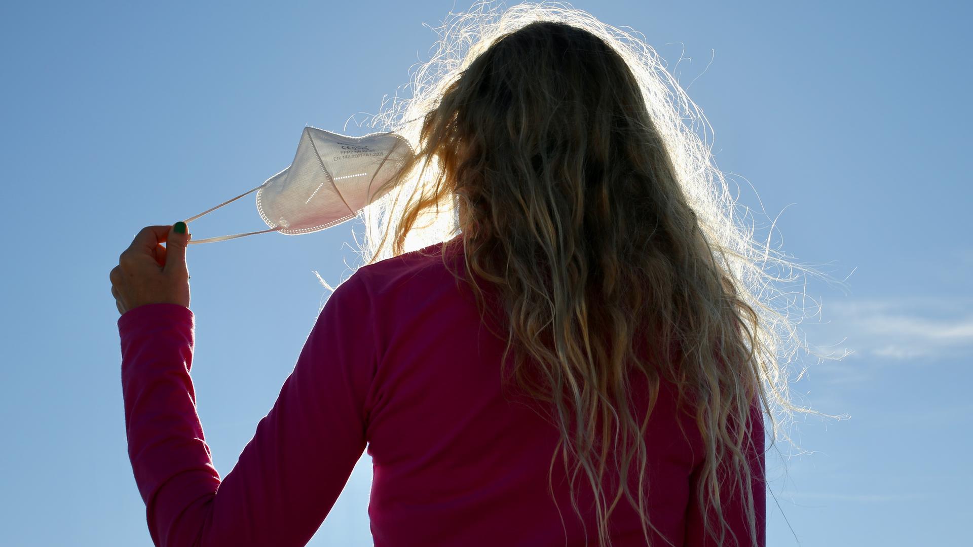 Frau von hinten zu sehen, zieht sich die Maske vom Gesicht