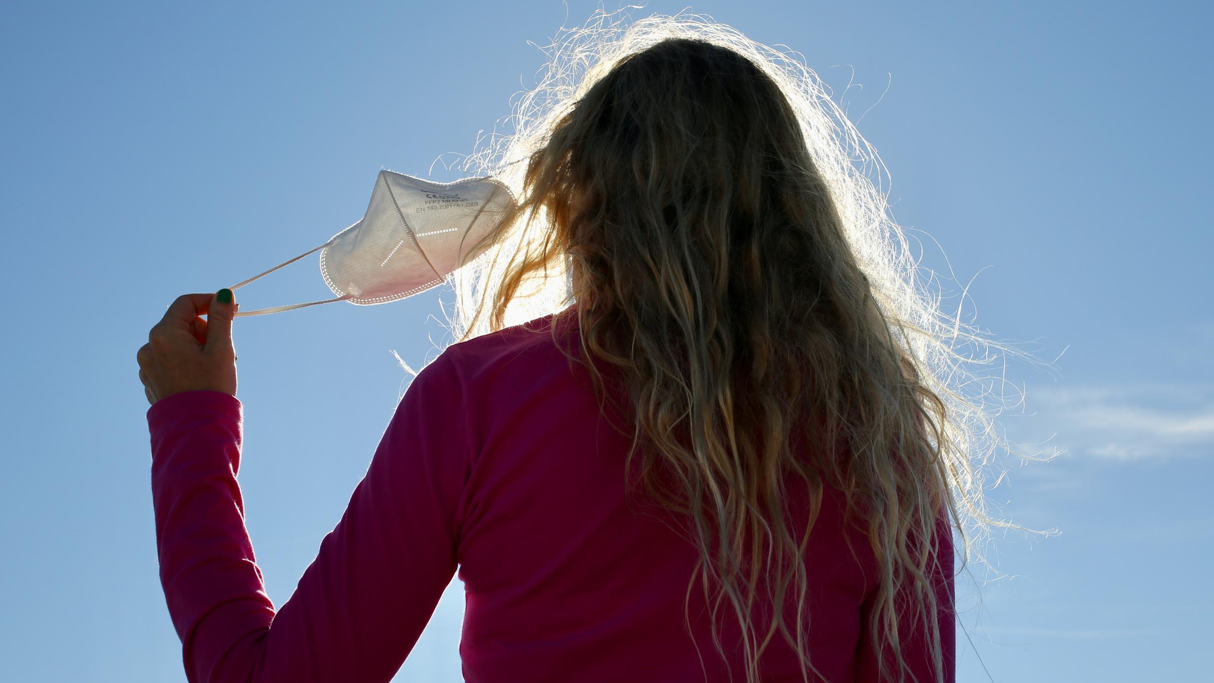 Frau von hinten zu sehen, zieht sich die Maske vom Gesicht