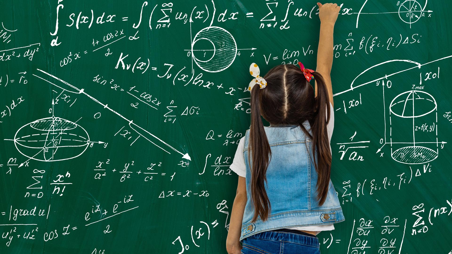Ein Mädchen vor einer Schultafel mit Matheformeln. 