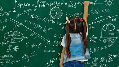 Ein Mädchen vor einer Schultafel mit Matheformeln. 