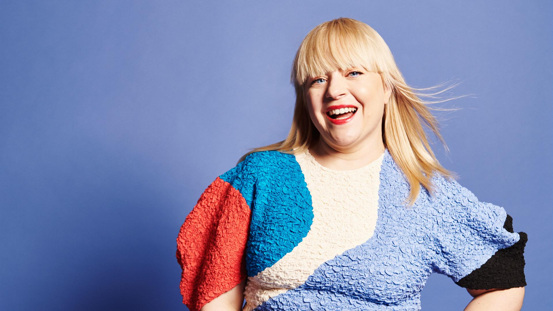 Eine Frau strahlt in die Kamera, sie trägt ein buntes Kleid. 