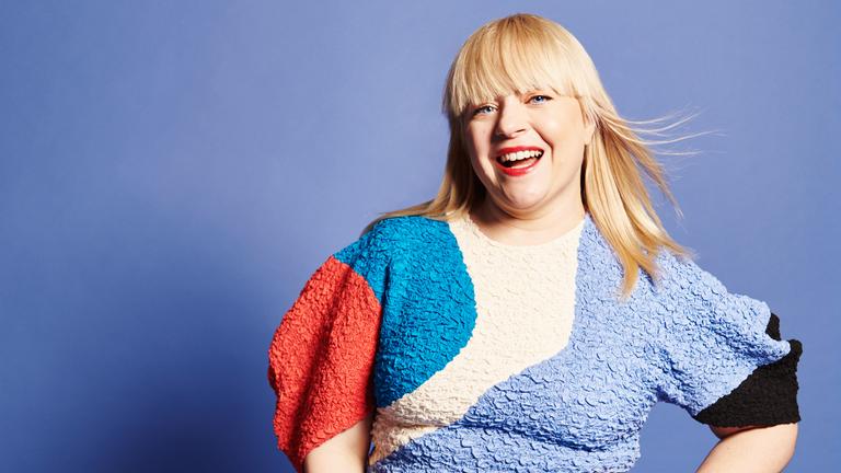 Eine Frau strahlt in die Kamera, sie trägt ein buntes Kleid. 