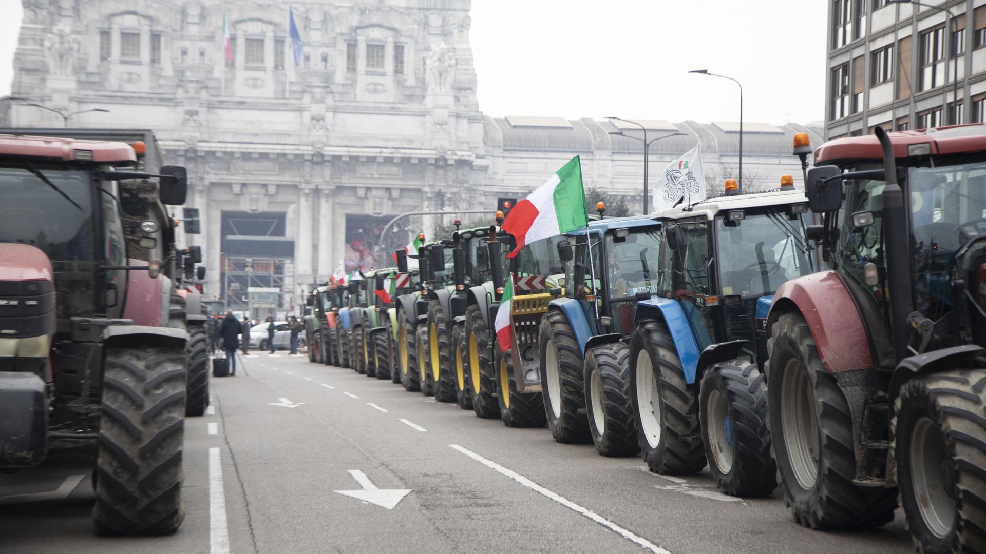 Traktoren stehen hintereinander auf einer Straße mit einer italienischen Flagge.