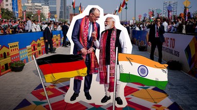 Merz und Modi stehen nebeneinander, auf ihnen eine Deutschlandflagge und eine Indienflagge