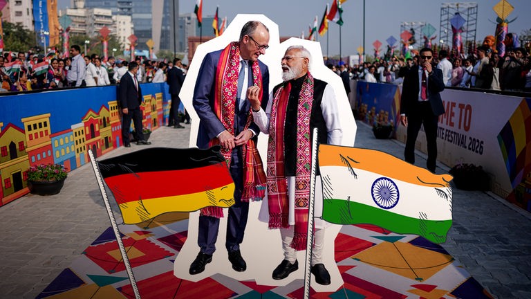 Merz und Modi stehen nebeneinander, auf ihnen eine Deutschlandflagge und eine Indienflagge