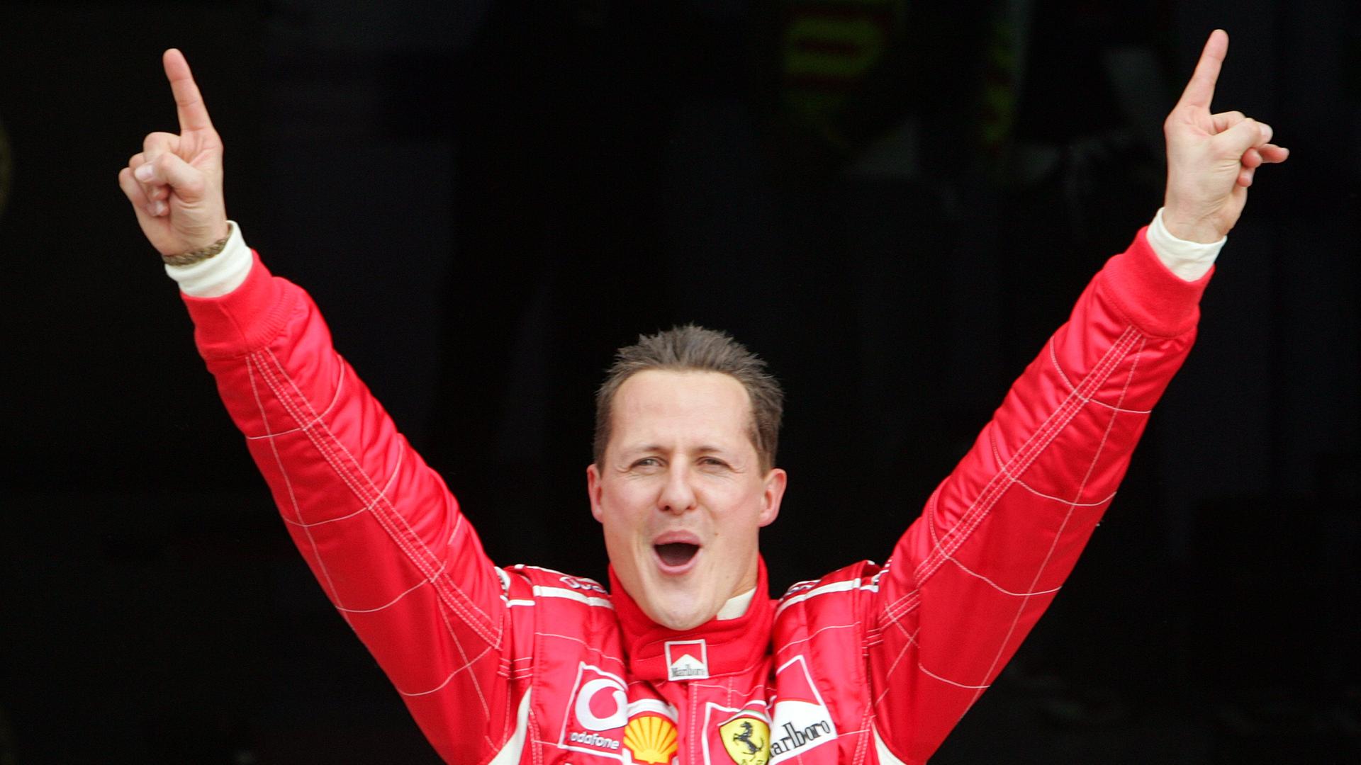 Auf dem Bild sieht man Michael Schumacher, wie er die Arme hochreißt und jubelt. 