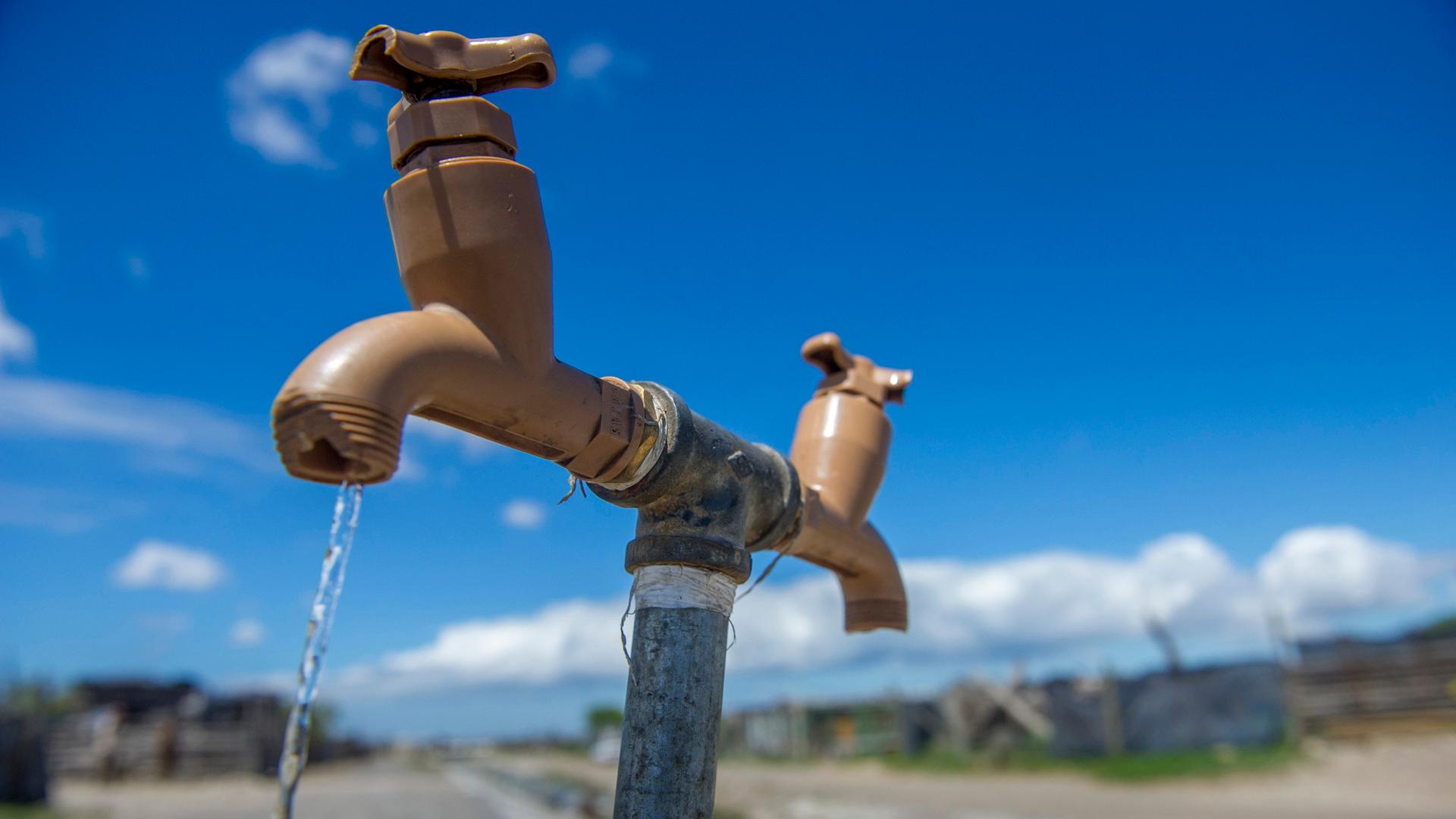 Symbolbild für Wasserknappheit: Wasserhahn im Feld. Trinkwasser fließt. 