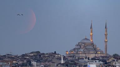 Die Hagia Sofia ist zu sehen im Morgengrauen, klarer H immel und eien leicht rötlich-orangefarben schimmernde Sichel des Mondes, über die ein Vogel fliegt.