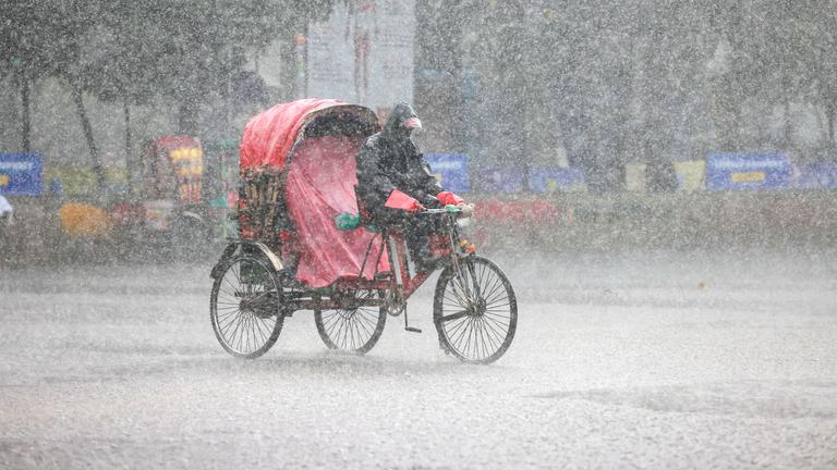 Menschen fahren während eines Monsun-Platzregens mit Rikschas durch Dhaka.