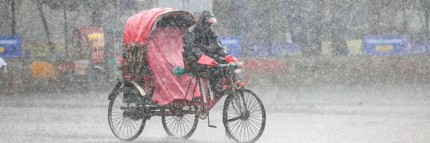 Menschen fahren während eines Monsun-Platzregens mit Rikschas durch Dhaka.